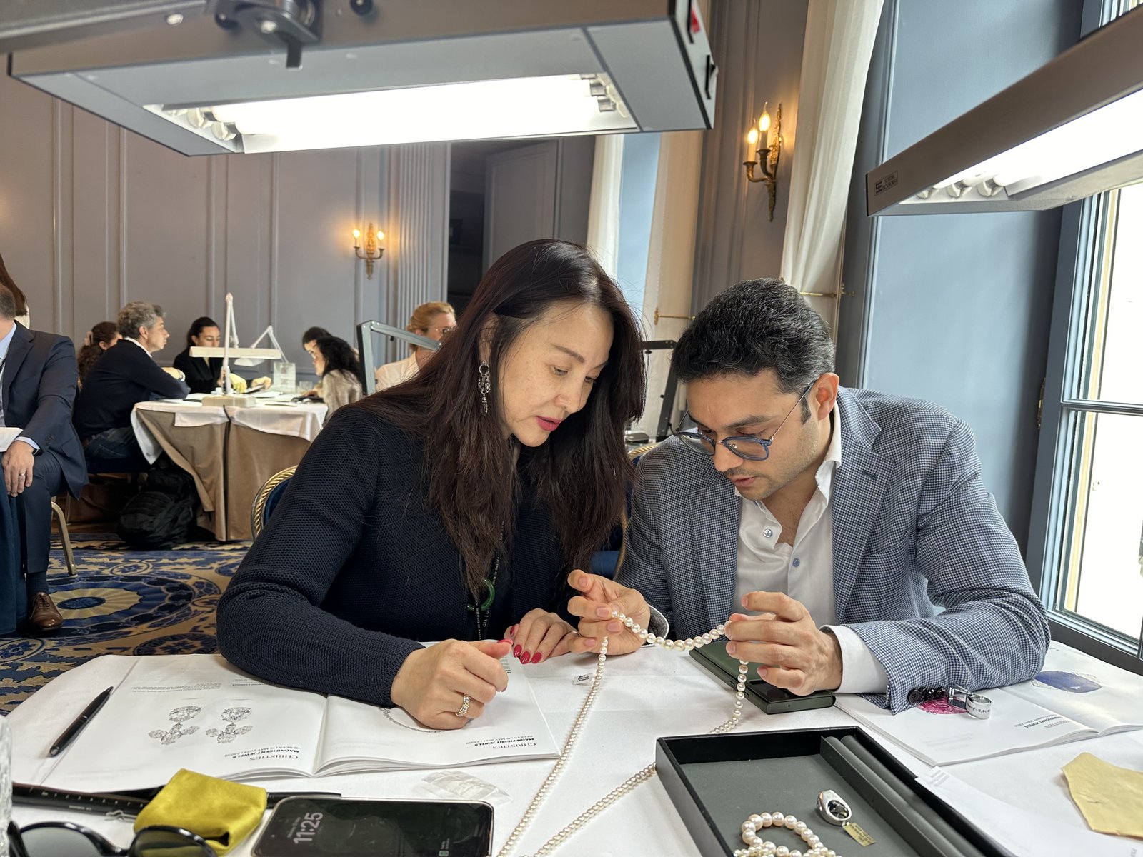 Kehan Li examining a row of natural pearl strands laid out on a white tablecloth at the auction preview.